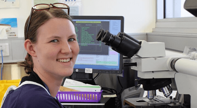 A woman in a lab coat smiles warmly at the camera, showcasing a friendly and professional demeanor.